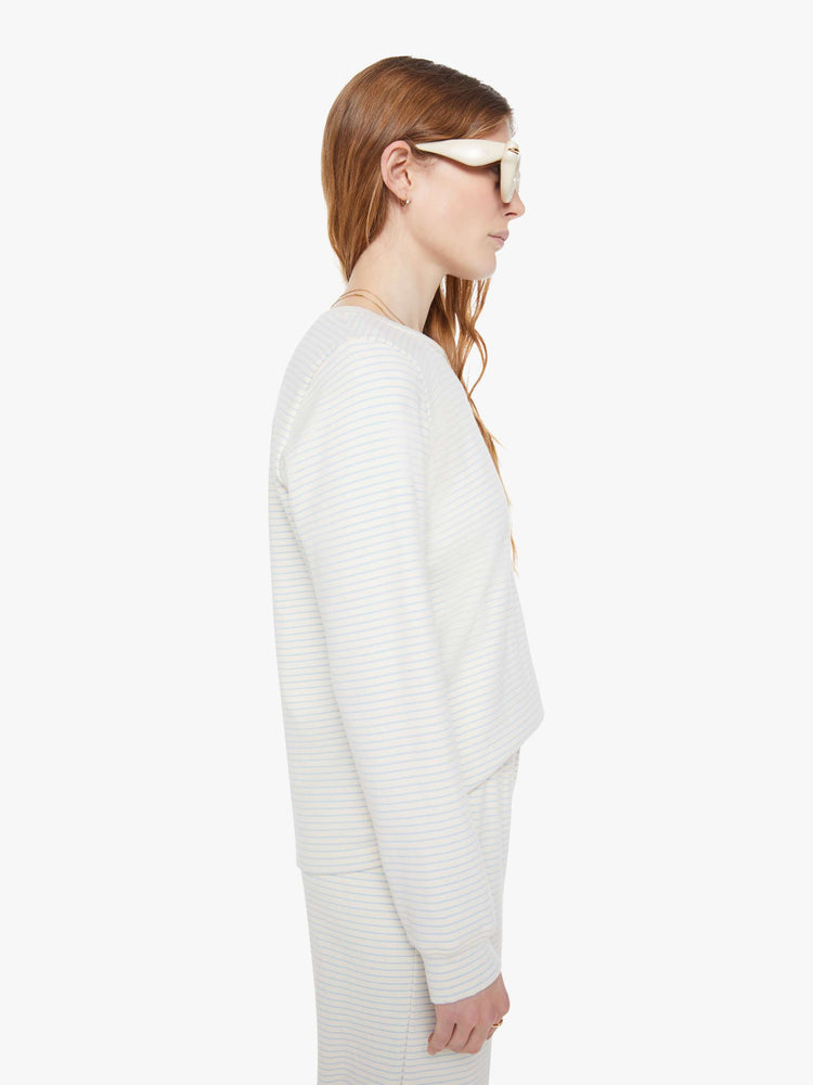 Side view of a woman in off-white with light blue horizontal stripes and a red M patch on the hem long sleeve tee.