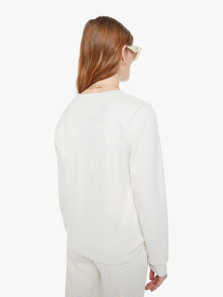 Back view of a woman in off-white with light blue horizontal stripes and a red M patch on the hem long sleeve tee.