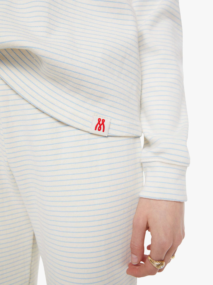 Close up view of a woman in off-white with light blue horizontal stripes and a red M patch on the hem long sleeve tee.