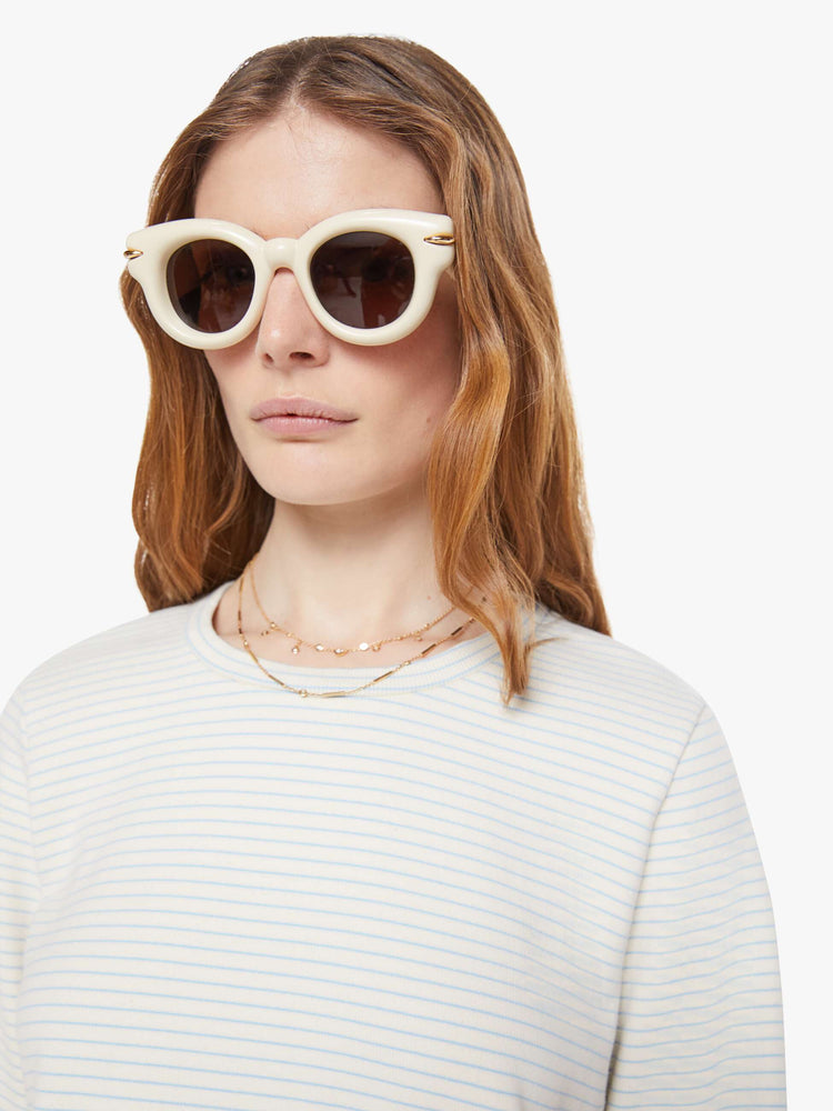 Close up view of a woman in off-white with light blue horizontal stripes and a red M patch on the hem long sleeve tee.