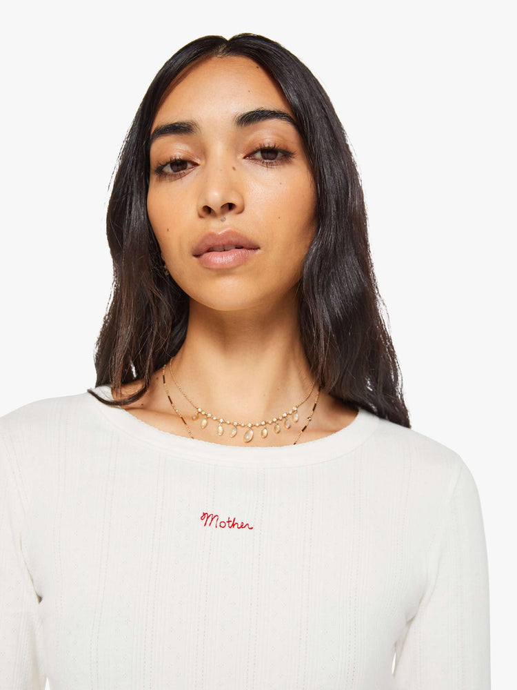Close up view of a woman in a white with MOTHER in red detail crewneck top with long sleeves and a narrow fit. 