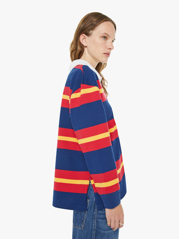 Side view of a woman in a shirt designed in red, navy and golden-yellow stripes with a fuzzy lamb patch on the chest.