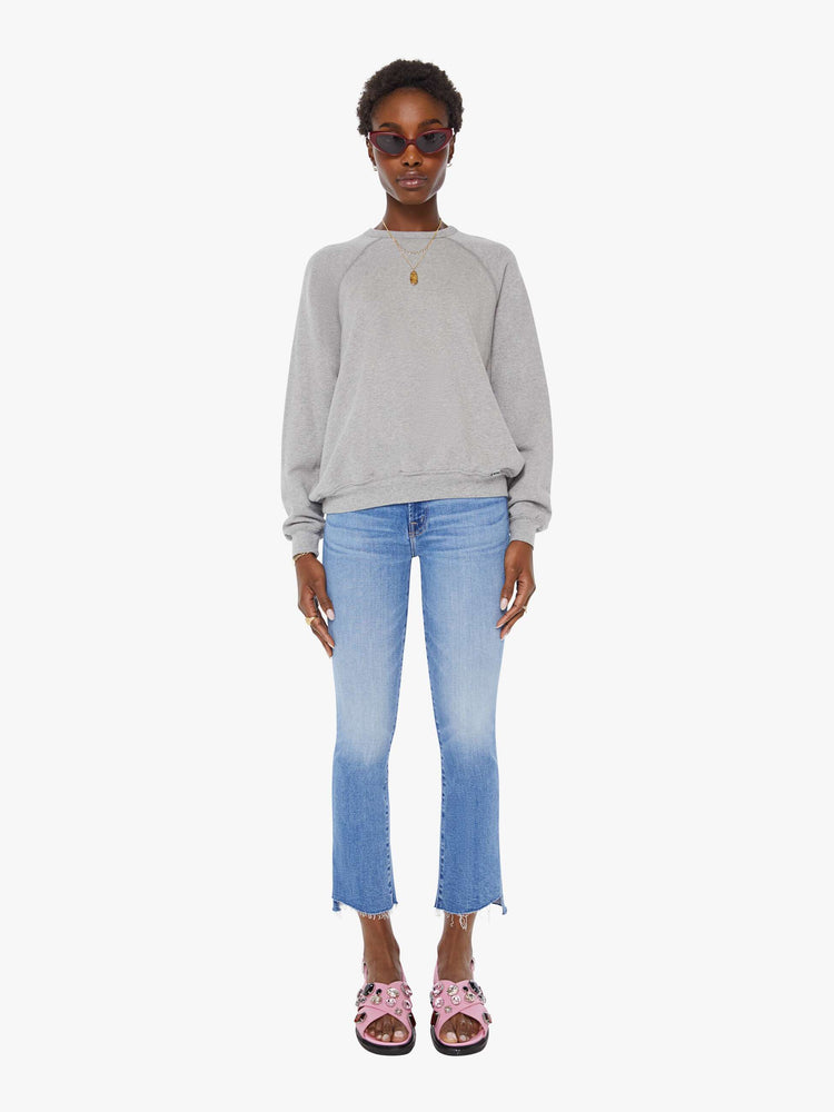 Front full body view of a woman in a grey oversized raglan sweatshirt with a crewneck, ribbed hems and a slightly cropped fit.