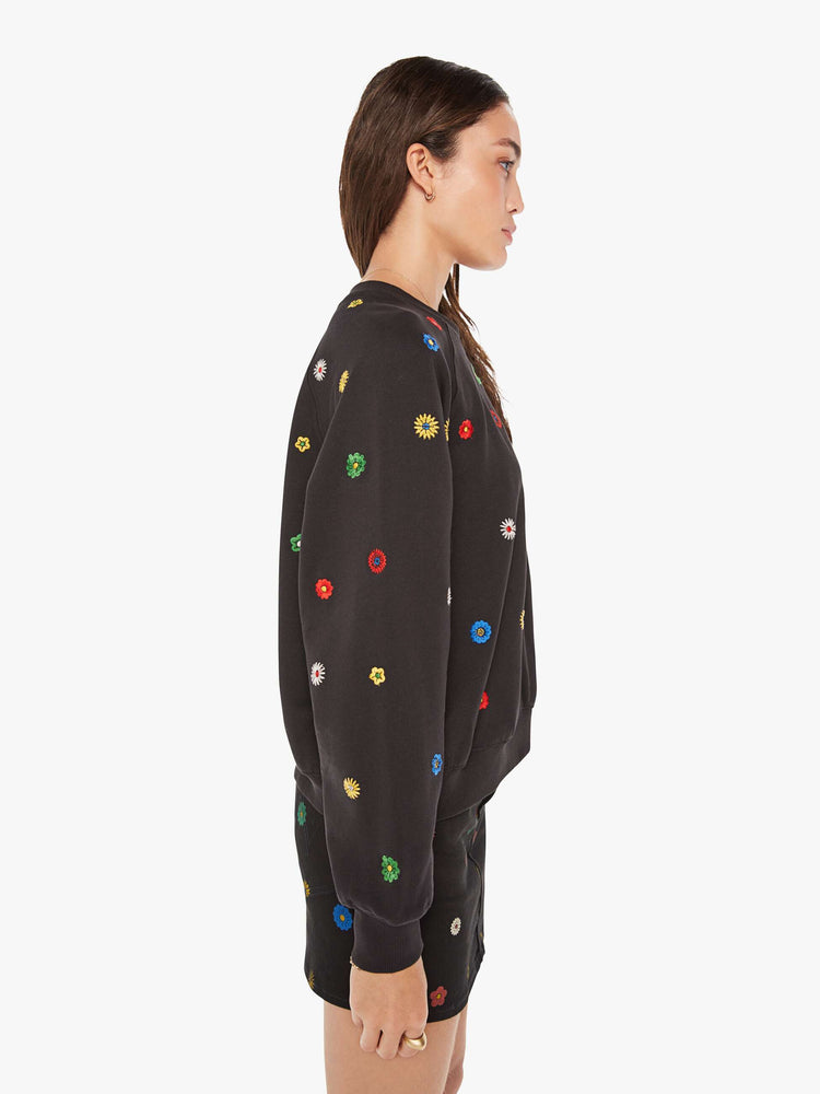Side view of a woman oversized sweatshirt in black with embroidered with colorful flowers throughout.
