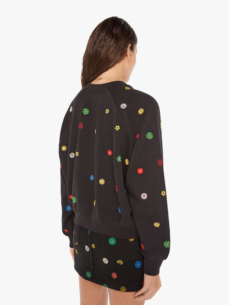 Back view of a woman oversized sweatshirt in black with embroidered with colorful flowers throughout.