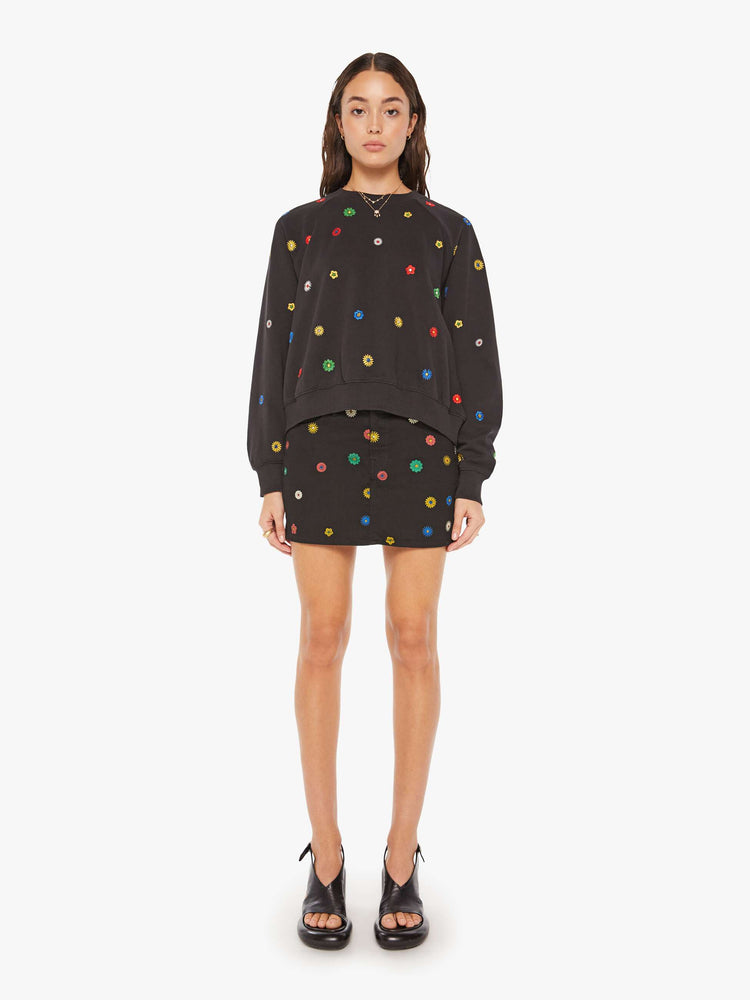 Full body view of a woman oversized sweatshirt in black with embroidered with colorful flowers throughout.