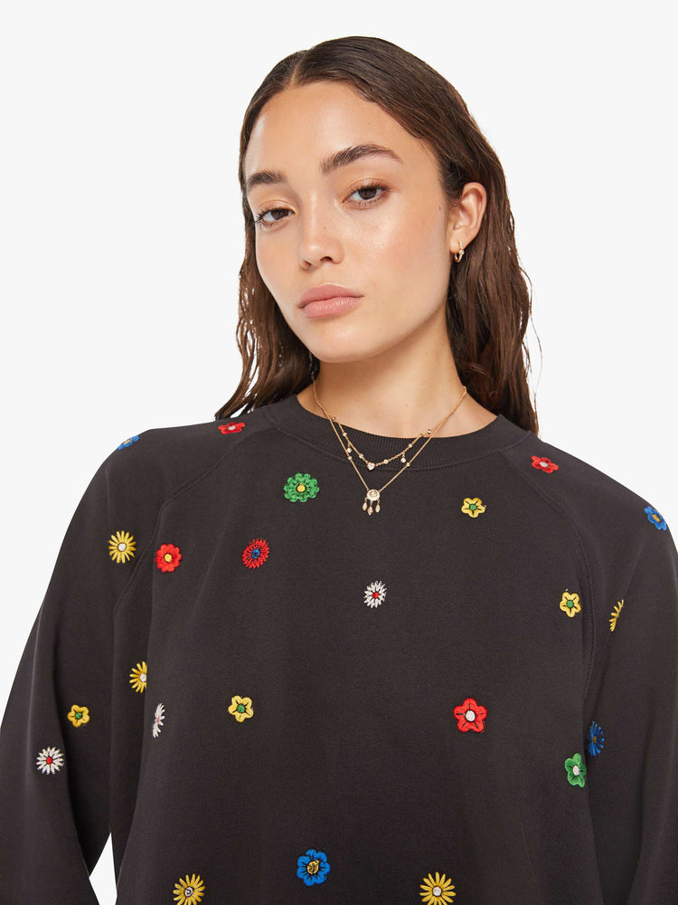 Close up view of a woman oversized sweatshirt in black with embroidered with colorful flowers throughout.