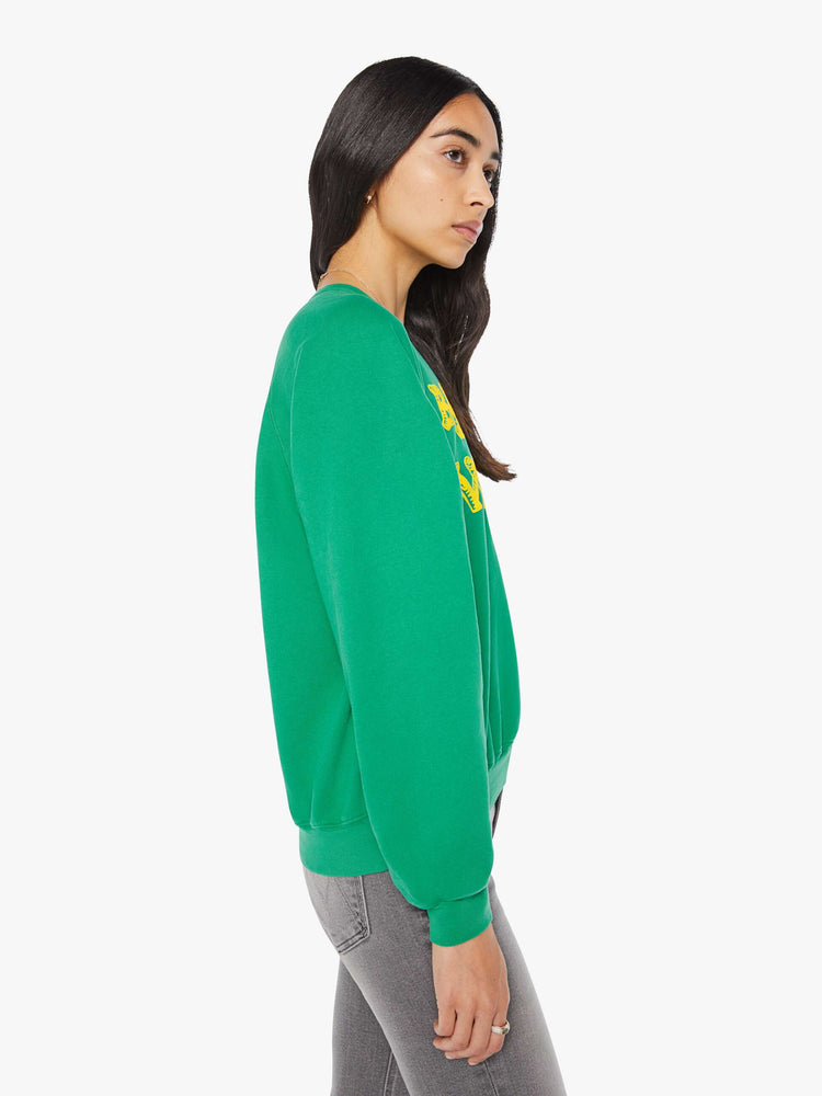 Side view of a woman in a green with yellow text on the front  oversized raglan sweatshirt.