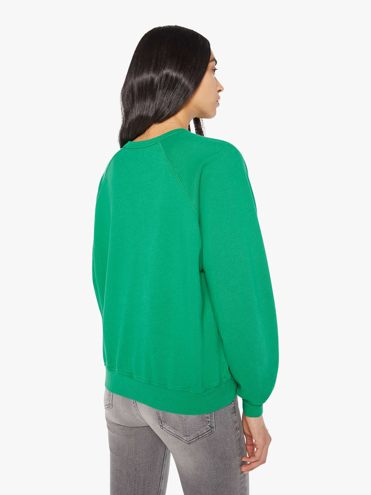 Back view of a woman in a green with yellow text on the front  oversized raglan sweatshirt.