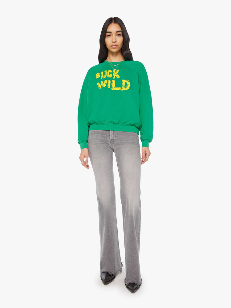 Full body view of a woman in a green with yellow text on the front  oversized raglan sweatshirt.