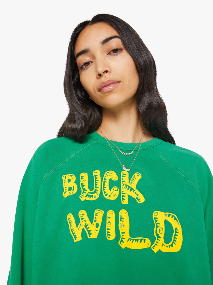 Close up view of a woman in a green with yellow text on the front  oversized raglan sweatshirt.