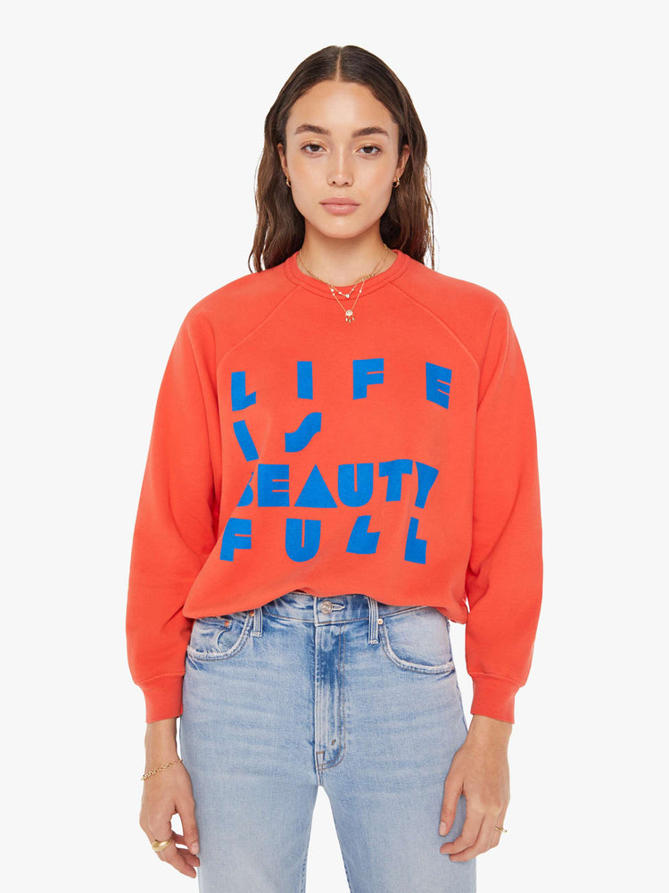 Front view of a woman in a oversized raglan sweatshirt with ribbed hems and slightly cropped fit in red with blue text graphic.