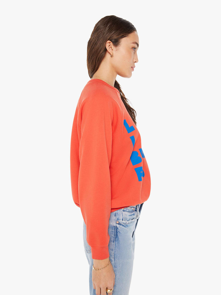 Side view of a woman in a oversized raglan sweatshirt with ribbed hems and slightly cropped fit in red with blue text graphic.