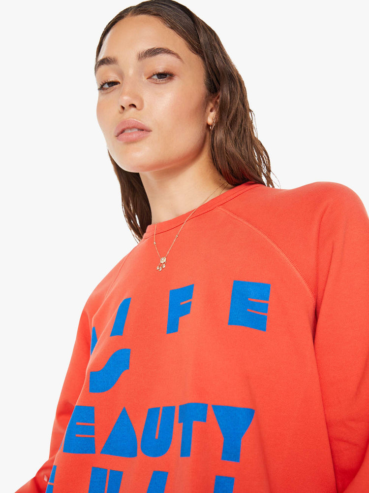 Close up view of a woman in a oversized raglan sweatshirt with ribbed hems and slightly cropped fit in red with blue text graphic.