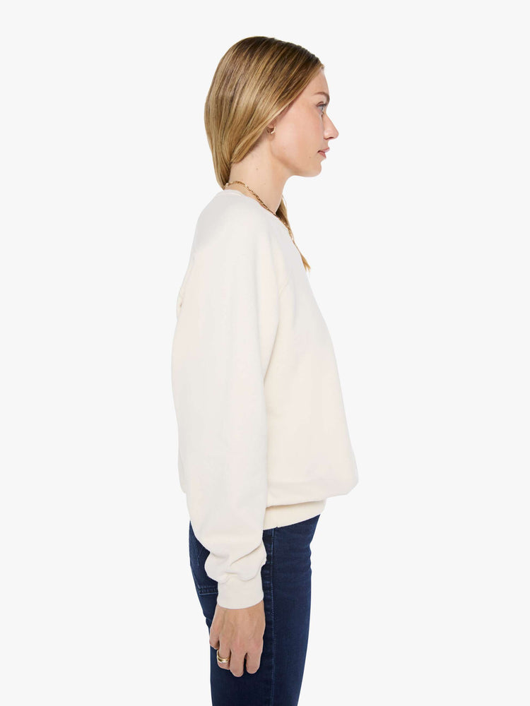 Side view of a woman in a cream oversized raglan sweatshirt with a crewneck, ribbed hems and a slightly cropped fit.