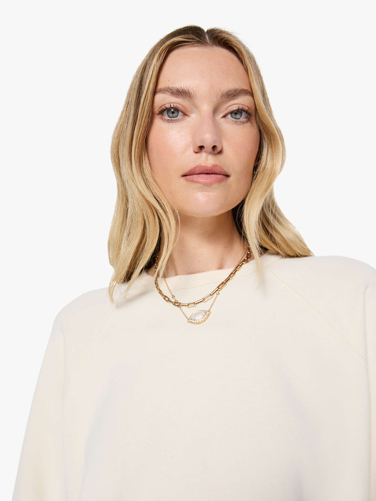 Close up view of a woman in a cream oversized raglan sweatshirt with a crewneck, ribbed hems and a slightly cropped fit.