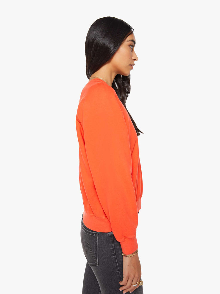 Side view of a woman in a bright orange  sweatshirt with a crewneck, ribbed hems and a slightly cropped fit. 