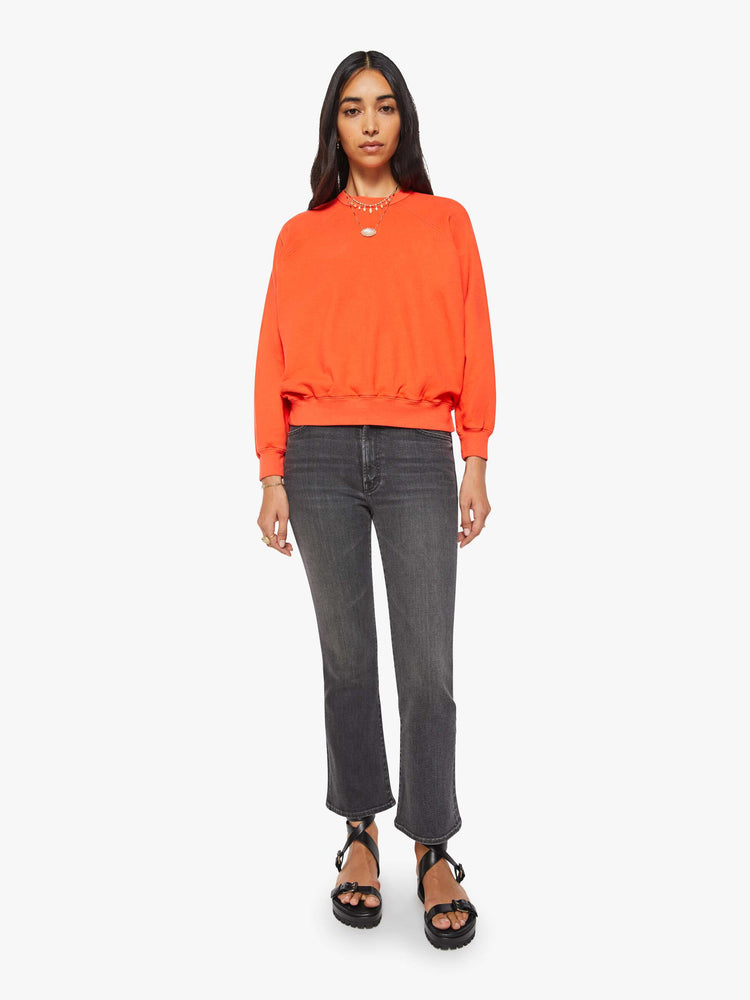 Full body view of a woman in a bright orange  sweatshirt with a crewneck, ribbed hems and a slightly cropped fit. 