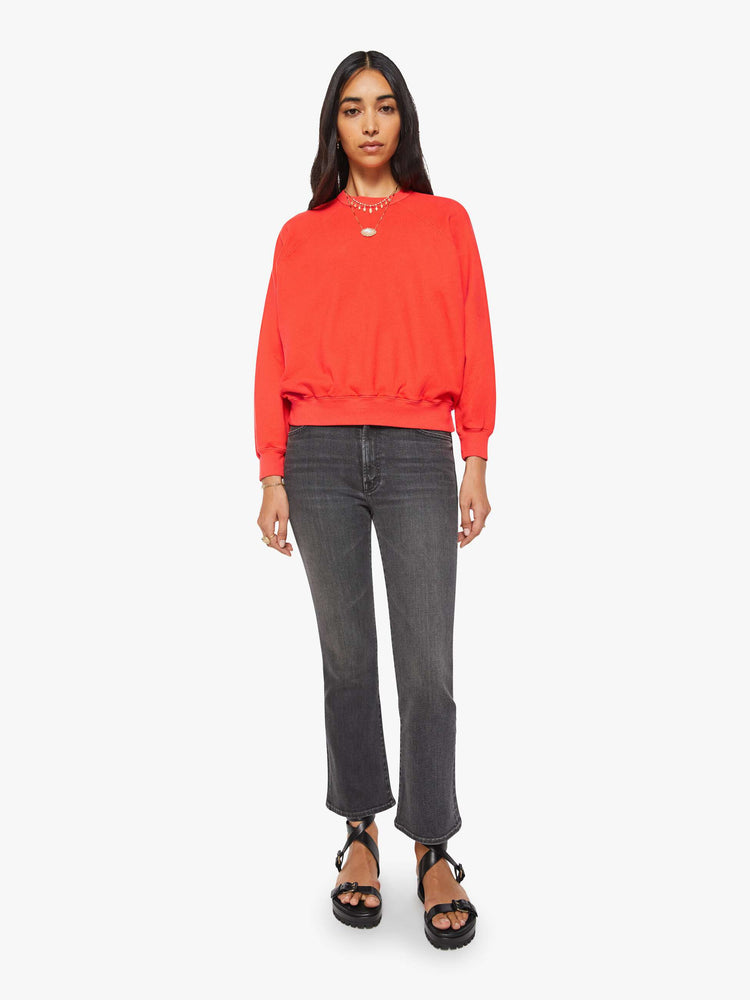 Full body view of a woman in a bright orange  sweatshirt with a crewneck, ribbed hems and a slightly cropped fit. 