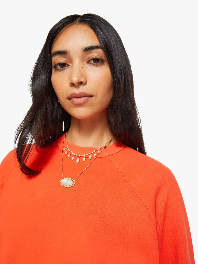 Close up view of a woman in a bright orange  sweatshirt with a crewneck, ribbed hems and a slightly cropped fit. 