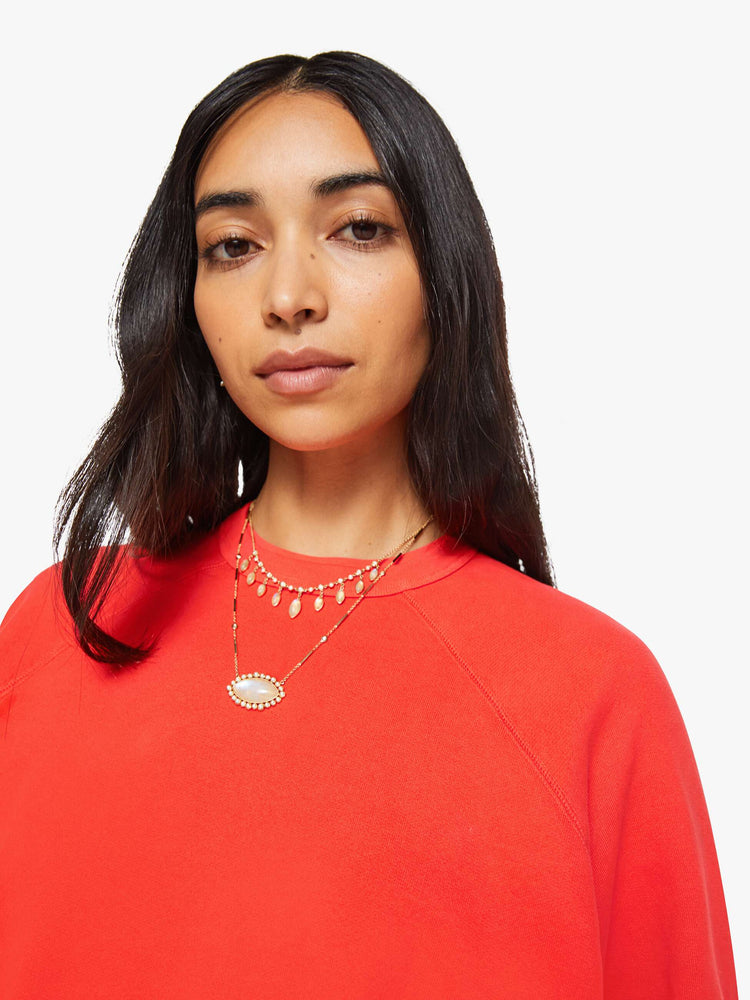 Close up view of a woman in a bright orange  sweatshirt with a crewneck, ribbed hems and a slightly cropped fit. 