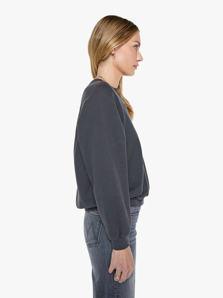 Side view of a woman in a faded black oversized raglan sweatshirt with a crewneck, ribbed hems and a slightly cropped fit.