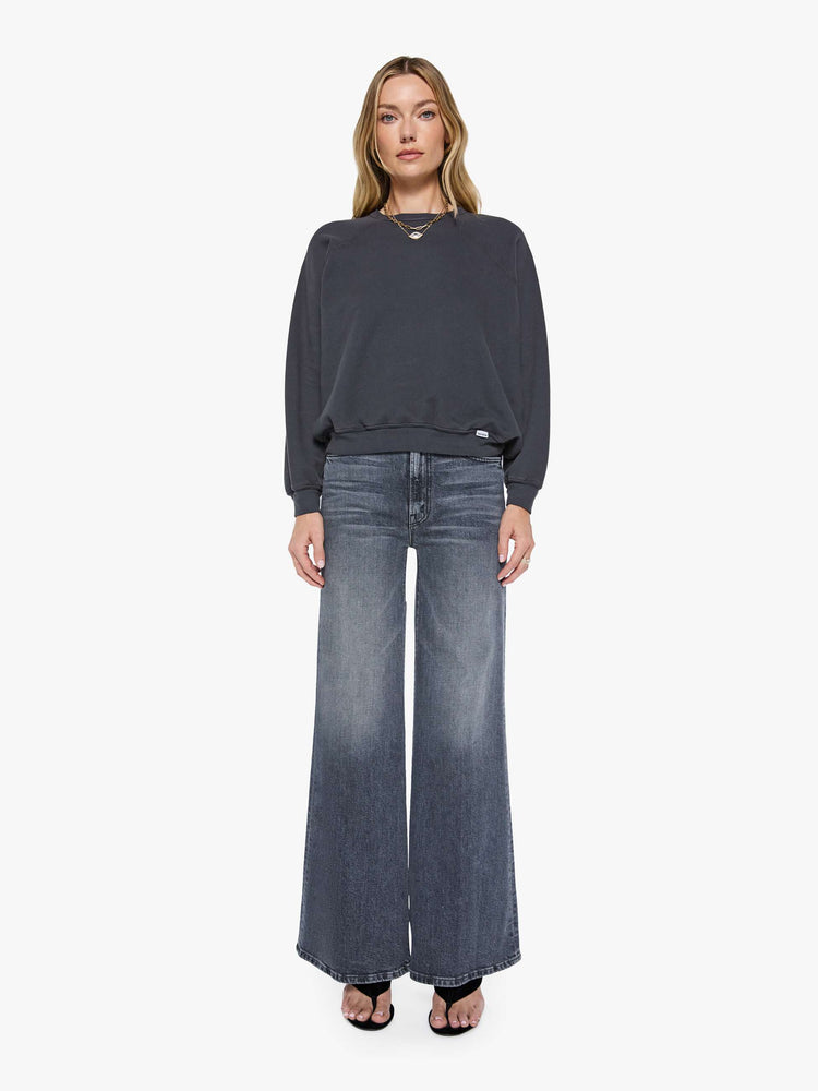 Full body view of a woman in a faded black oversized raglan sweatshirt with a crewneck, ribbed hems and a slightly cropped fit.