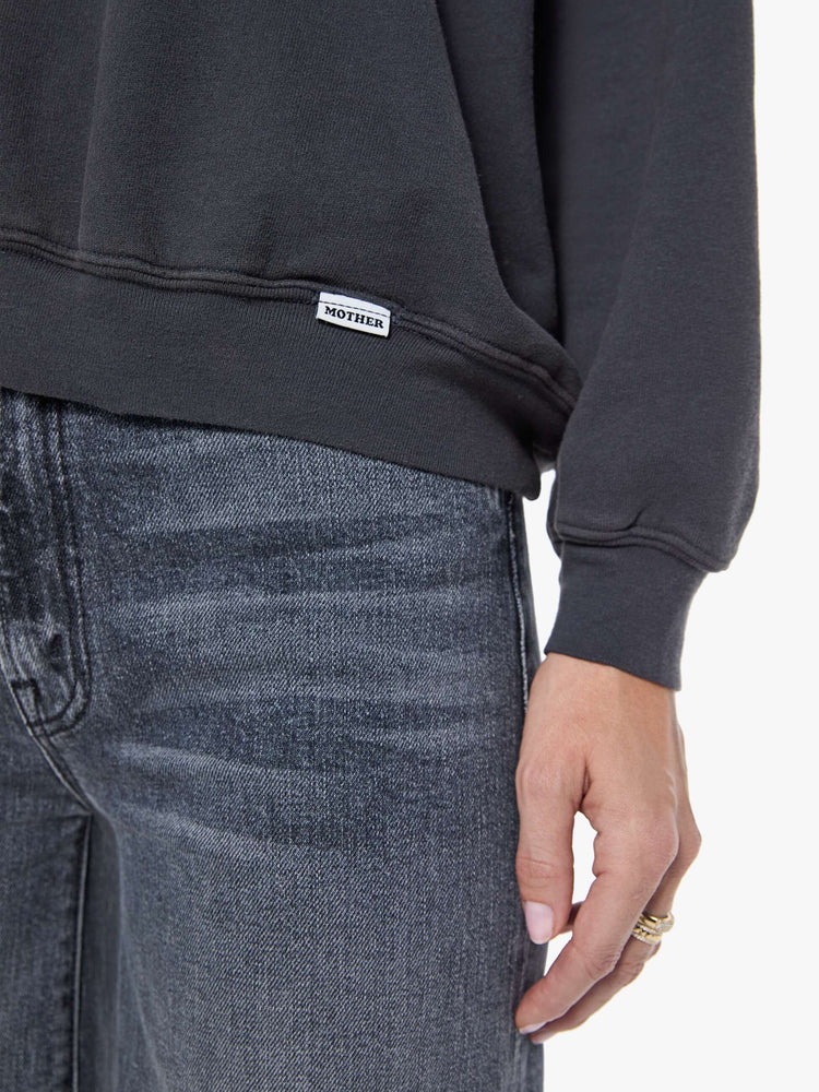 Close up view of a woman in a faded black oversized raglan sweatshirt with a crewneck, ribbed hems and a slightly cropped fit.