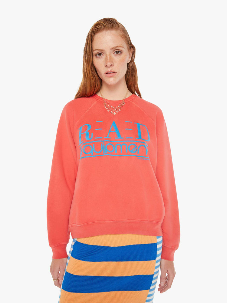 A front body view of a woman wearing a faded red sweatshirt in an oversized fit, featuring a bright blue graphic reading "RAD equipment", worn over a colorful knit dress.