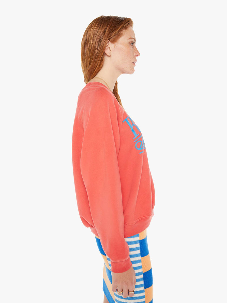 A side body view of a woman wearing a faded red sweatshirt in an oversized fit, worn over a colorful knit dress.