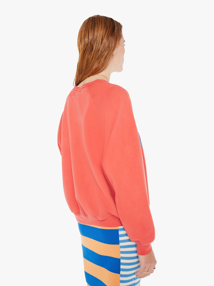 A back body view of a woman wearing a faded red sweatshirt in an oversized fit, worn over a colorful knit dress.