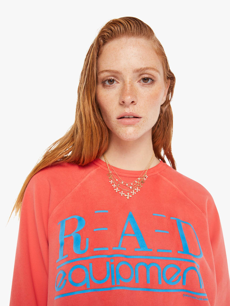 A front close up view of a woman wearing a faded red sweatshirt in an oversized fit, featuring a bright blue graphic reading "RAD equipment".