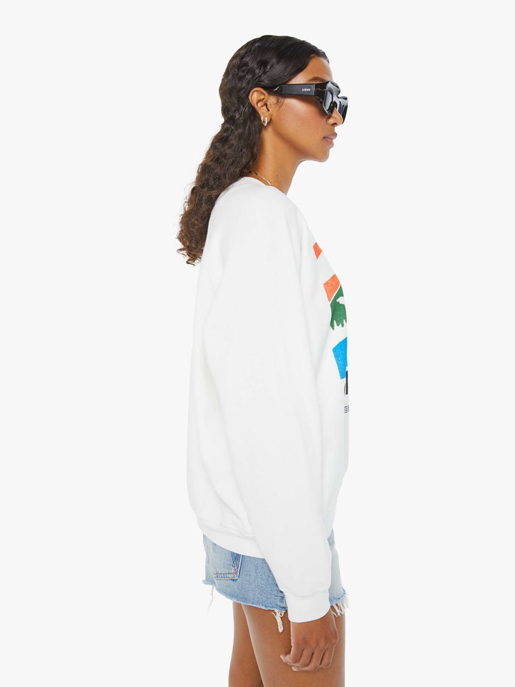 Side view of a woman in an oversized white raglan crewneck sweatshirt, with ribbed hems and a slightly cropped fit designed with a vintage-inspired St. Tropez graphic on the front.