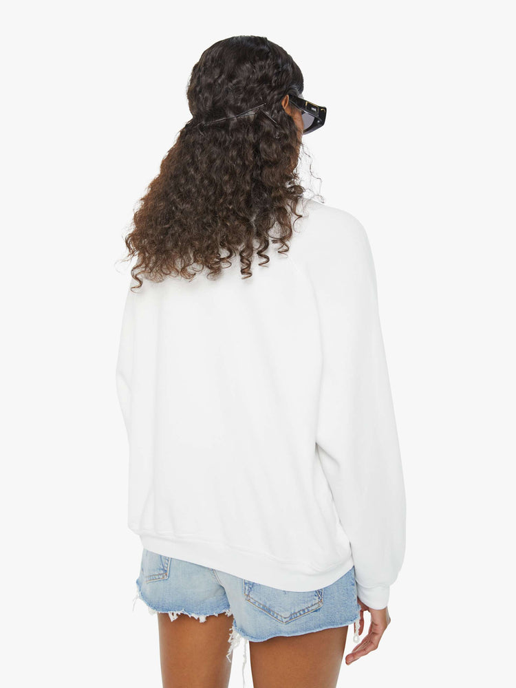 Back view of a woman in an oversized white raglan crewneck sweatshirt, with ribbed hems and a slightly cropped fit designed with a vintage-inspired St. Tropez graphic on the front.