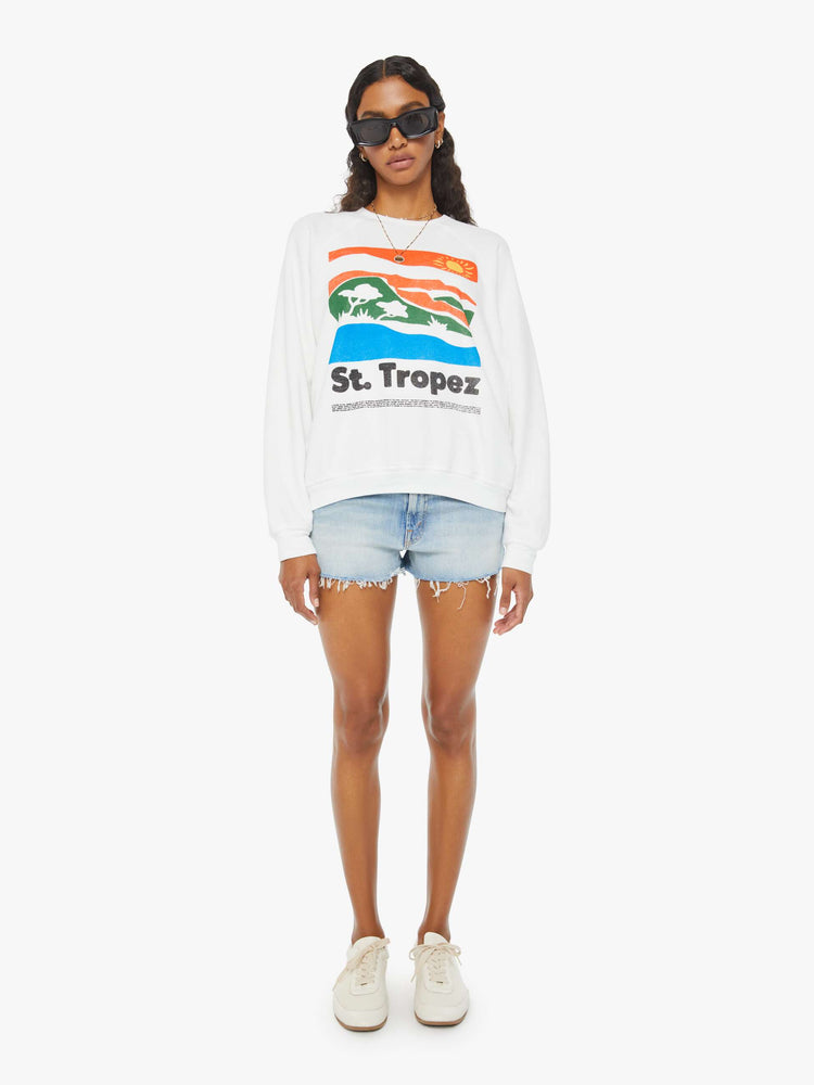 Full front view of a woman in an oversized white raglan crewneck sweatshirt, with ribbed hems and a slightly cropped fit designed with a vintage-inspired St. Tropez graphic on the front.