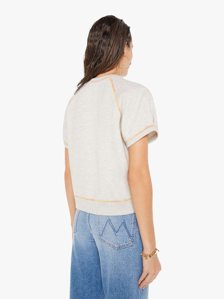 A back view of a woman wearing  a light heather grey crew neck sweatshirt featuring short raglan sleeves, a cropped body, and contrast orange thread, paired with medium blue jeans.
