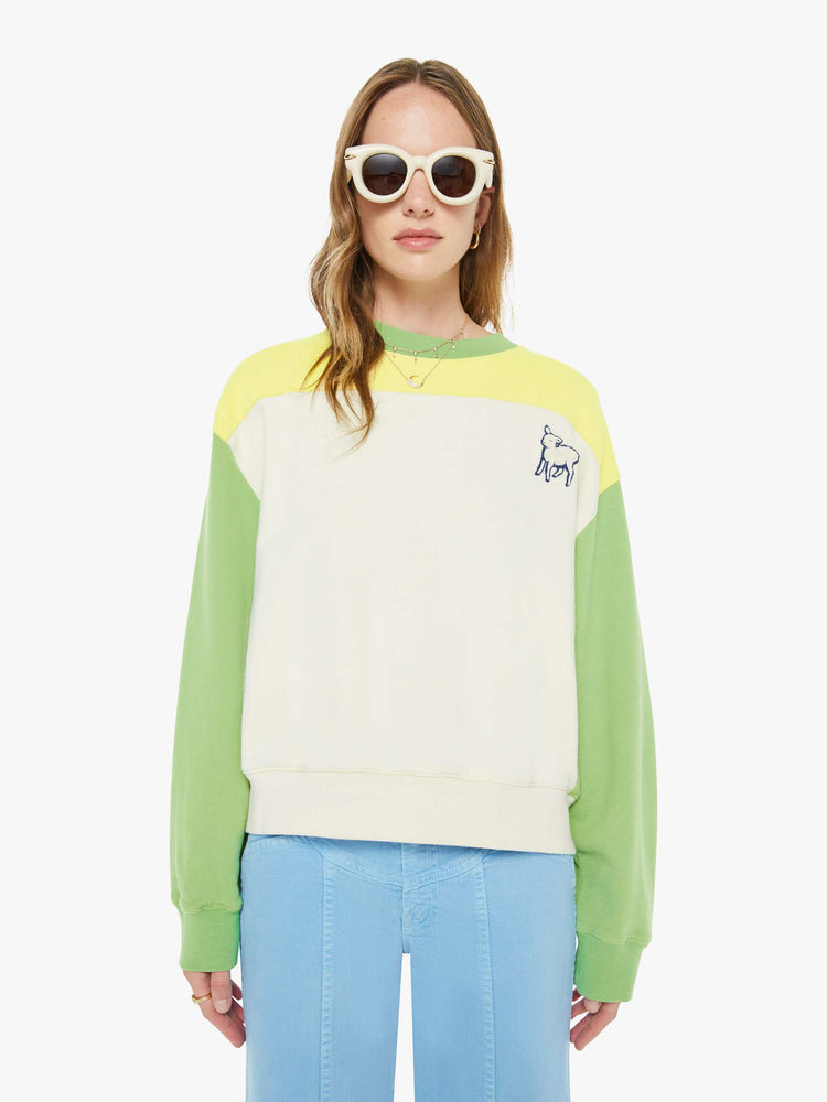 Front view of a woman in an off-white with a yellow panel across the chest sweatshirt, green sleeves and trim and a fuzzy lamb patch on the chest.