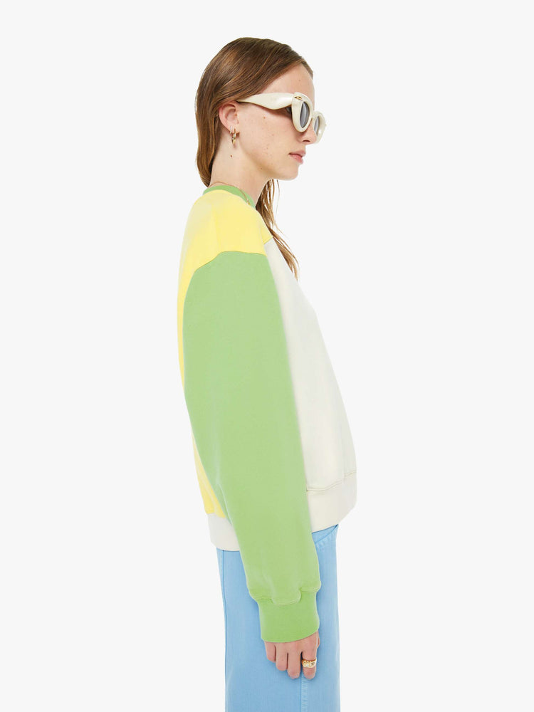 Side view of a woman in an off-white with a yellow panel across the chest sweatshirt, green sleeves and trim and a fuzzy lamb patch on the chest.