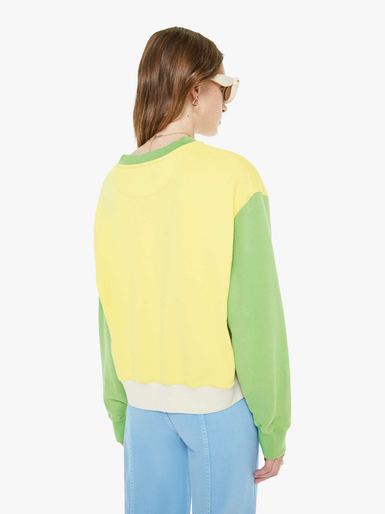 Back view of a woman in an off-white with a yellow panel across the chest sweatshirt, green sleeves and trim and a fuzzy lamb patch on the chest.