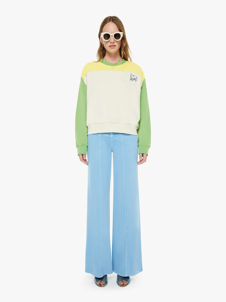 Full body view of a woman in an off-white with a yellow panel across the chest sweatshirt, green sleeves and trim and a fuzzy lamb patch on the chest.