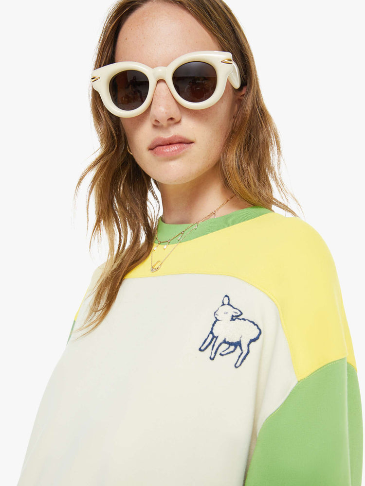 Close up view of a woman in an off-white with a yellow panel across the chest sweatshirt, green sleeves and trim and a fuzzy lamb patch on the chest.
