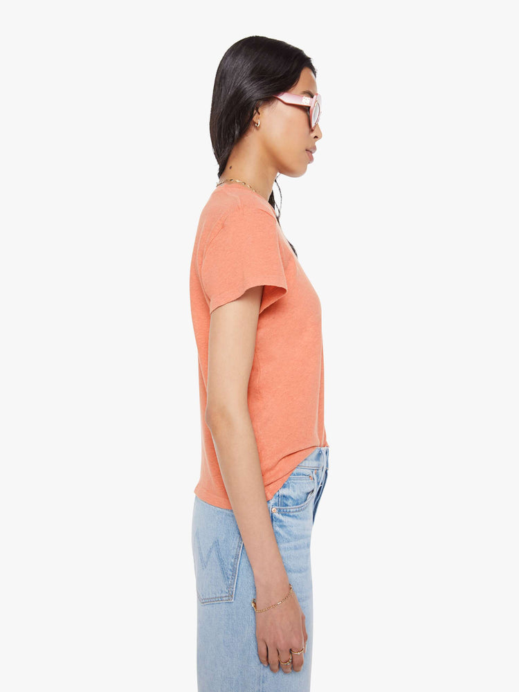 Side view of a woman in a faded orange tee with a cream text graphic on the front.