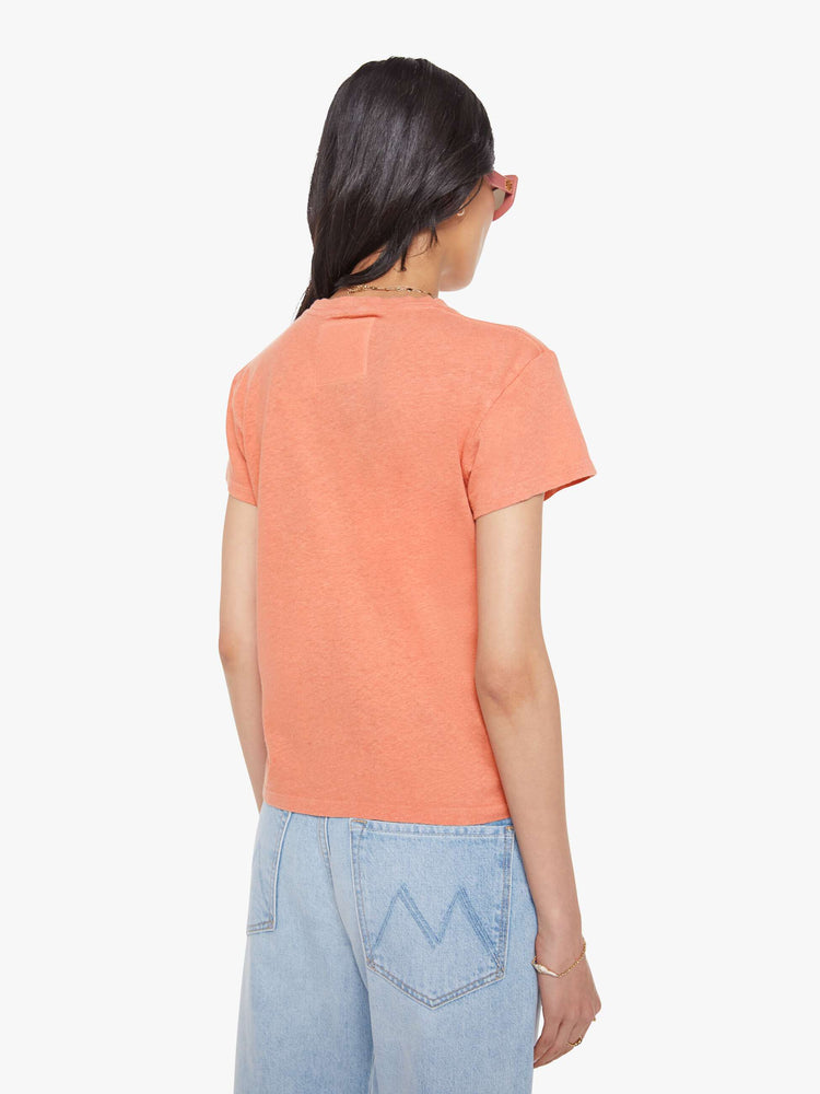 Back view of a woman in a faded orange tee with a cream text graphic on the front.