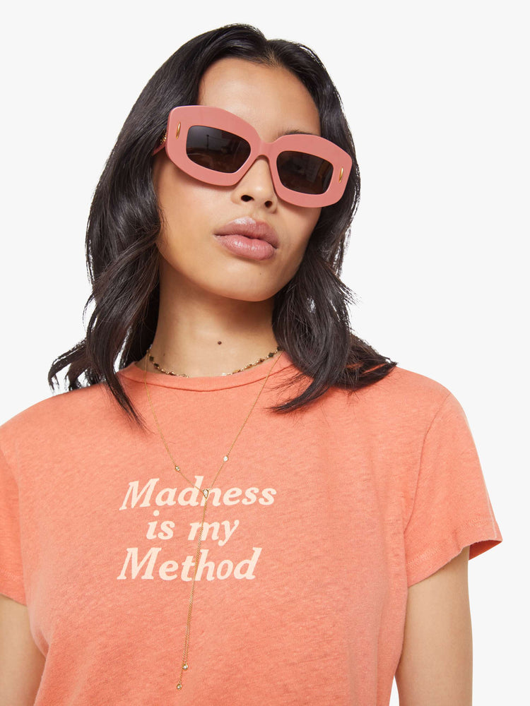 Close up view of a woman in a faded orange tee with a cream text graphic on the front.