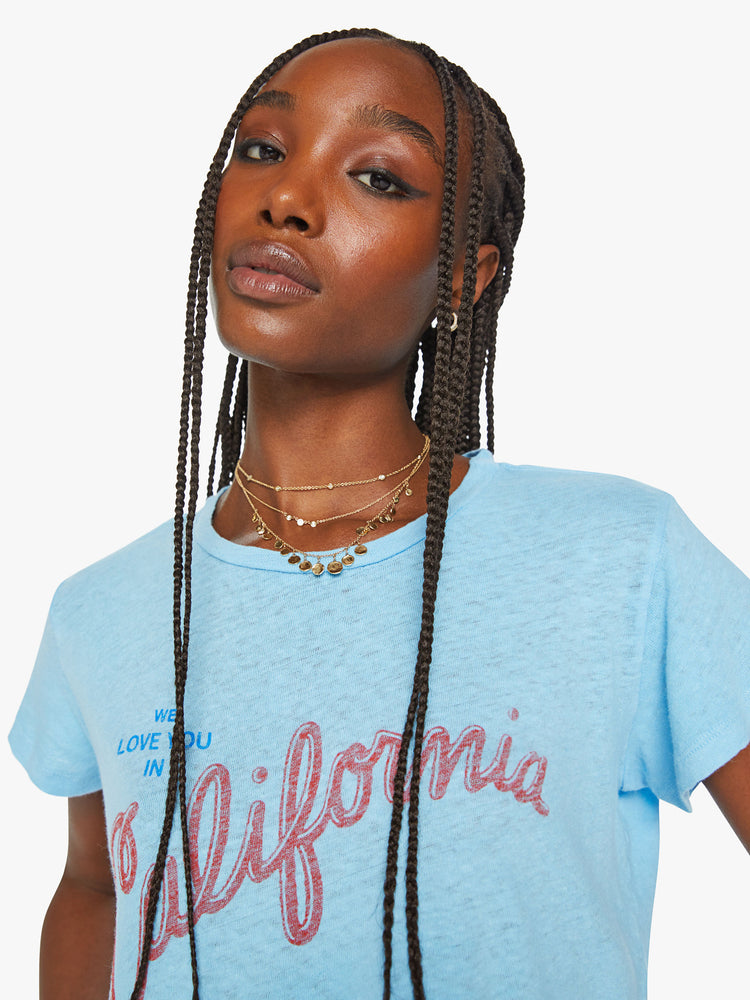 Close up view of a woman crewneck with a slim fit in sky blue, the knit tee pays homage to the Golden State with a red and blue text graphic across the chest.