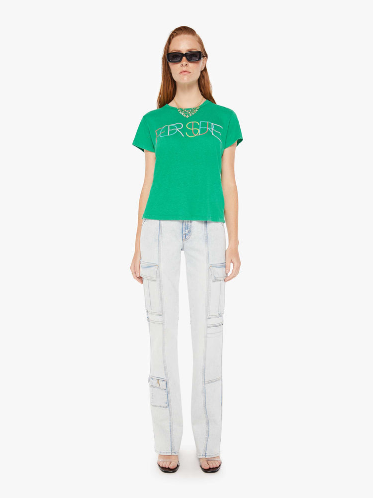A front full body view of a woman wearing a green crew neck tee featuring a colorful graphic reading "FOR SURE", paired with a light blue wash jean.