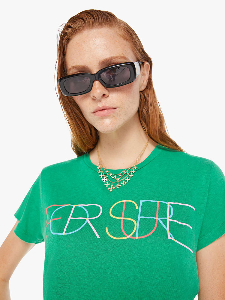 A front close up view of a woman wearing a green crew neck tee featuring a colorful graphic reading "FOR SURE".
