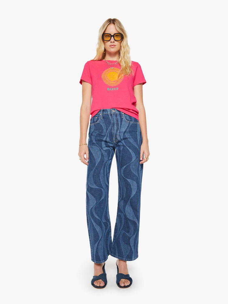 Full body view of a woman in a pink tee with golden sun graphic and text in teal on the front.
