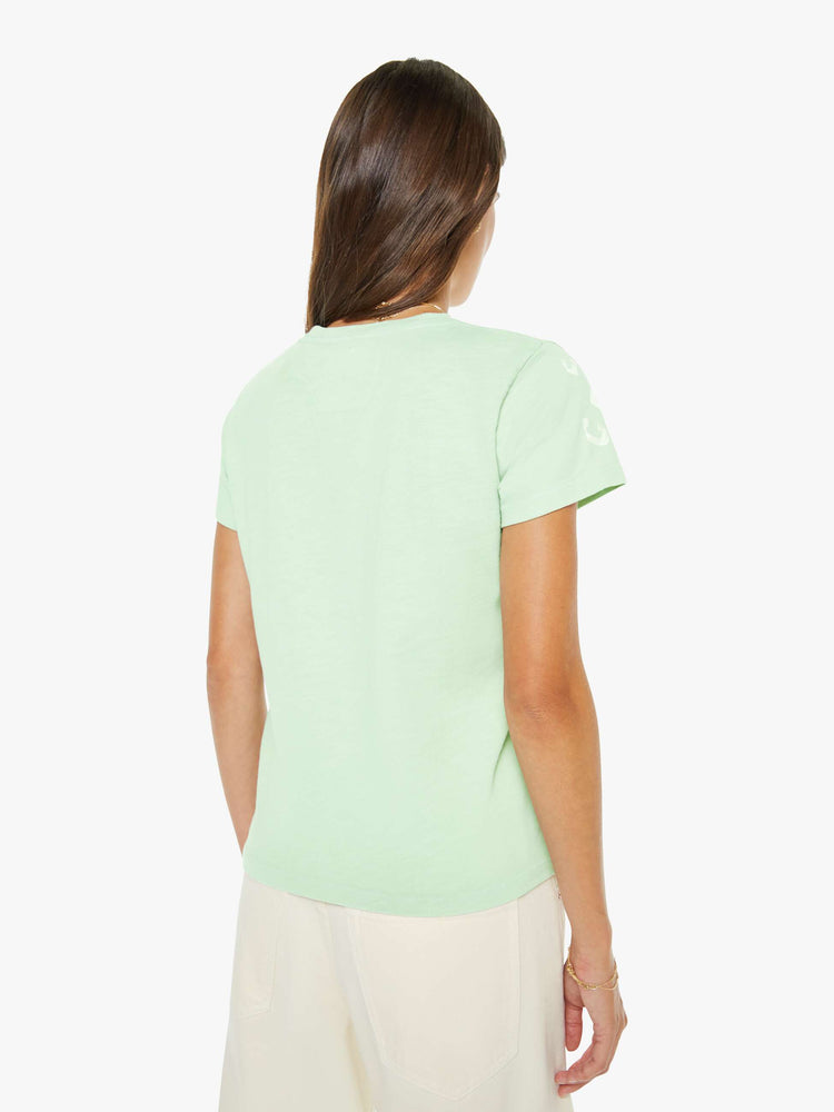 Back view of a woman in a light green tee with a list of ingredients in faded off-white text on the front.