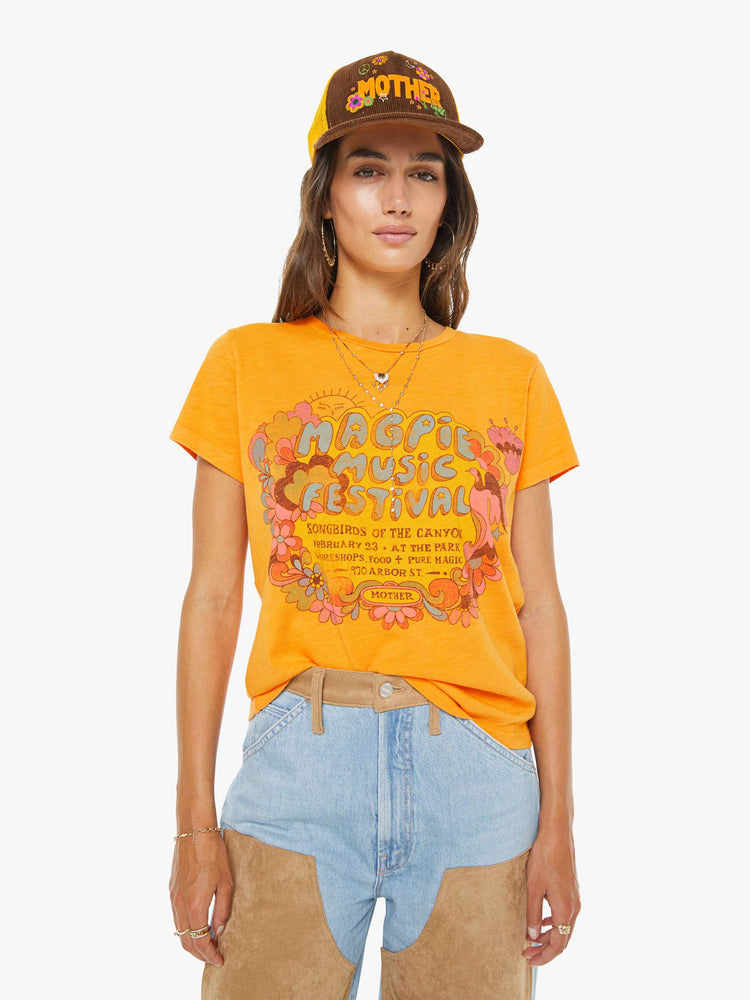 Front view of a woman in a golden yellow tee features a Magpie Music Festival graphic on the front with hand-drawn floral doodles.